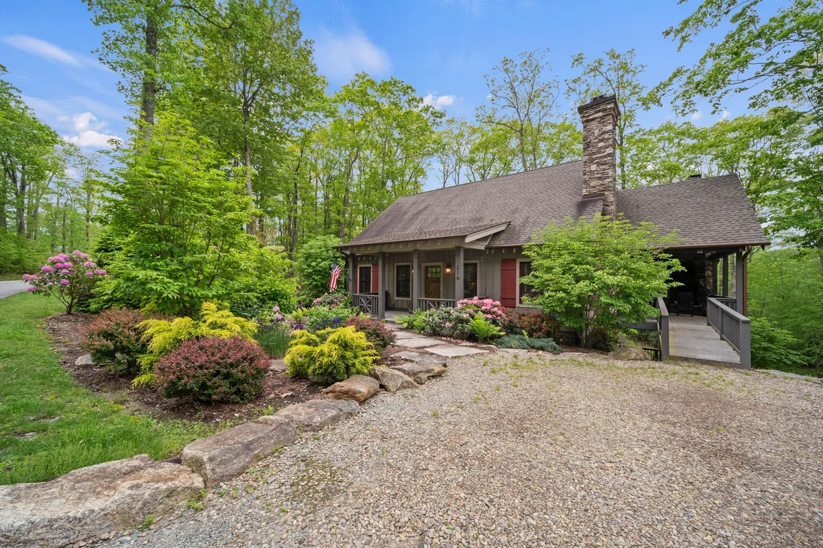 This image captures the front porch of Sweet Retreat, framed by a stone chimney, colorful flower beds, and a gravel path. The lush landscaping and inviting porch convey a warm, serene atmosphere, perfect for welcoming groups in any season.