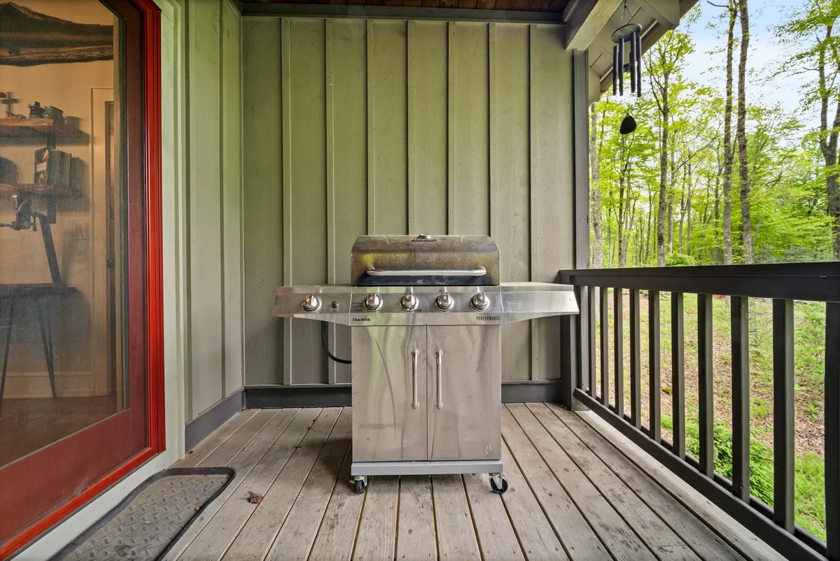 A wooden deck set among green trees, equipped with a top-of-the-line grill and plenty of space for outdoor entertaining. The scene suggests an inviting spot for barbecues, al fresco lunches, and socializing amid the natural surroundings.