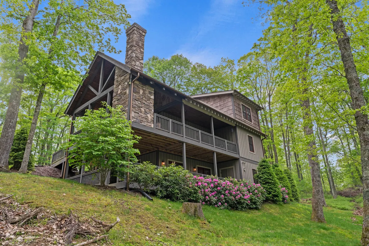 This image provides another exterior view, showcasing the stone chimney, front porch, and colorful flowering shrubs. The welcoming atmosphere invites guests (and their dogs) to relax or set off on scenic walks and hikes in the surrounding area.