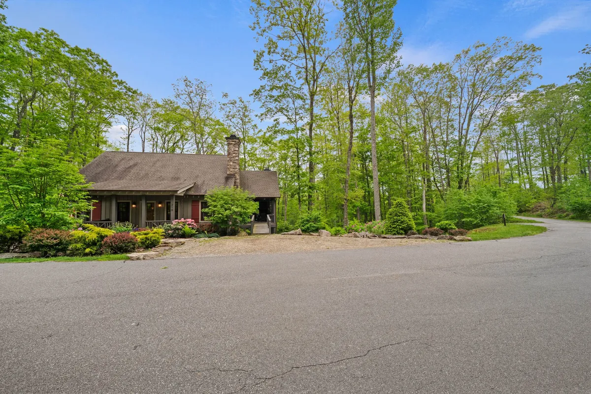This image captures the house nestled amid lush greenery, with a view of the surrounding landscape and the driveway. The scene exudes tranquility and a strong sense of immersion in nature, highlighting the proximity to trails and outdoor spaces right outside the front door.