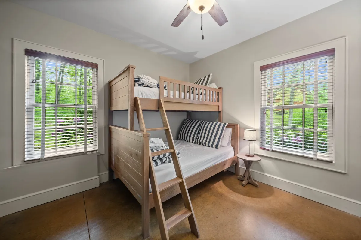 A cheerful bunk room with a striped bunk bed and windows that flood the space with natural light. The playful vibe is complemented by cozy bedding and a relaxed mood, inviting children or teens to make memories together.