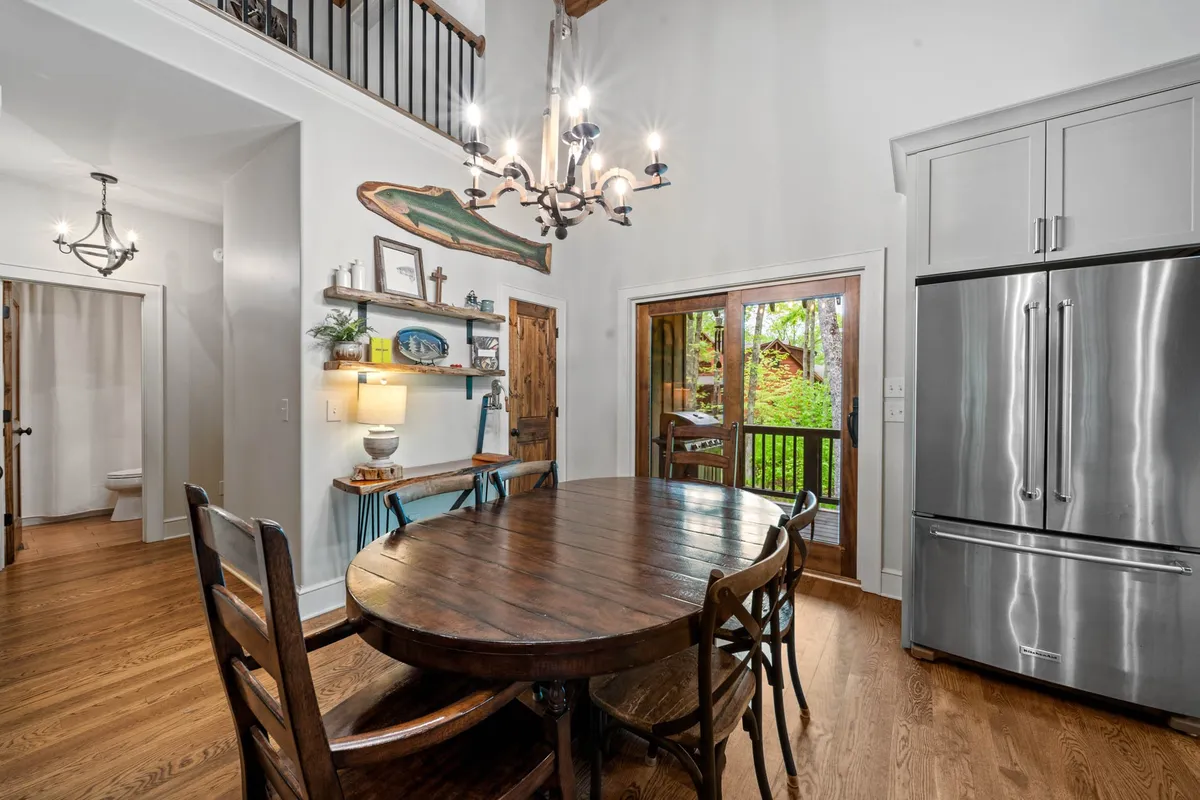 A warm, inviting dining area is highlighted, featuring a wooden table beneath a chandelier. The open door reveals easy access to the outdoors, and shelves with tasteful decor enhance the upscale vibe. The space is clearly designed for family gatherings and entertaining, while also connecting visually and physically to the scenery beyond.