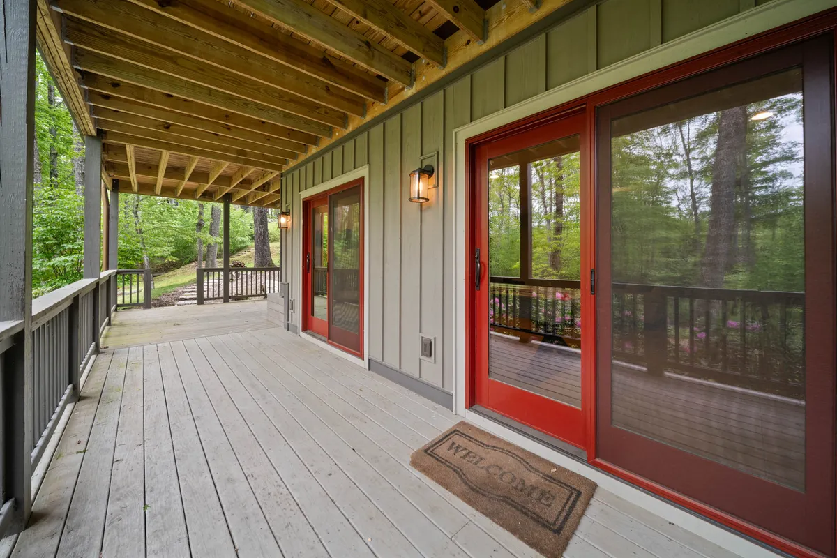 A close-up of the home's red doors, welcome mat, and wooden railing, set against a background of towering trees. The entryway exudes warmth and hospitality, inviting guests to explore both the home and its surroundings.
