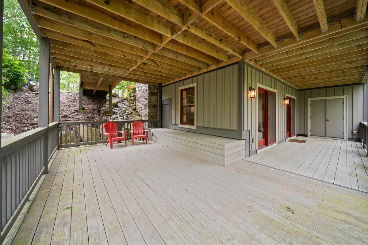 A wooden deck featuring red chairs overlooks rich greenery, inviting relaxation and offering an outdoor vantage point for enjoying the serene environment. The setting suggests a perfect spot for resting after outdoor activities or soaking in seasonal views.